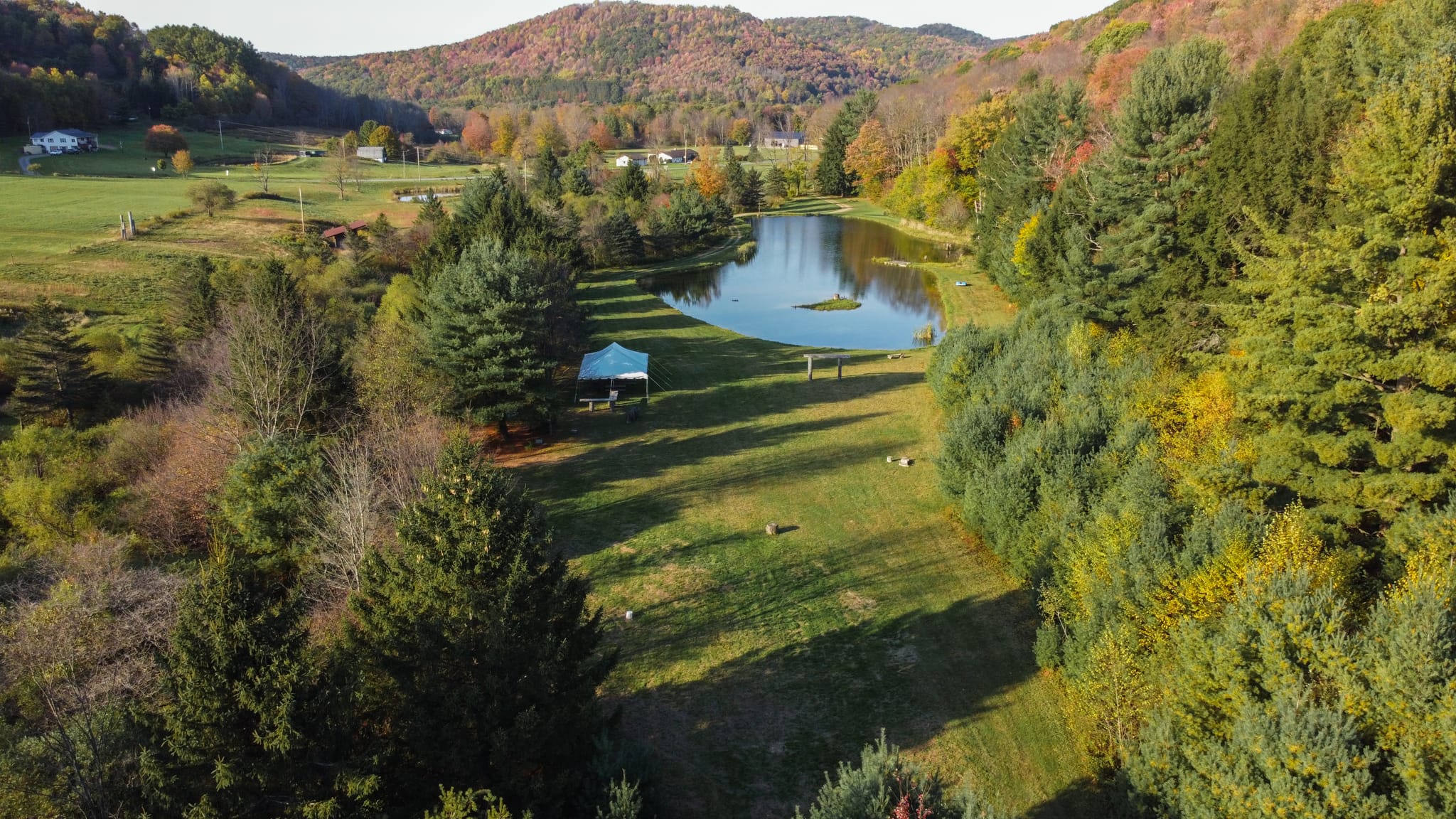 DJI_0616 Clara Creek Company, Scenic aerial view of a pond surrounded by fall foliage and a tent on a grassy field.
