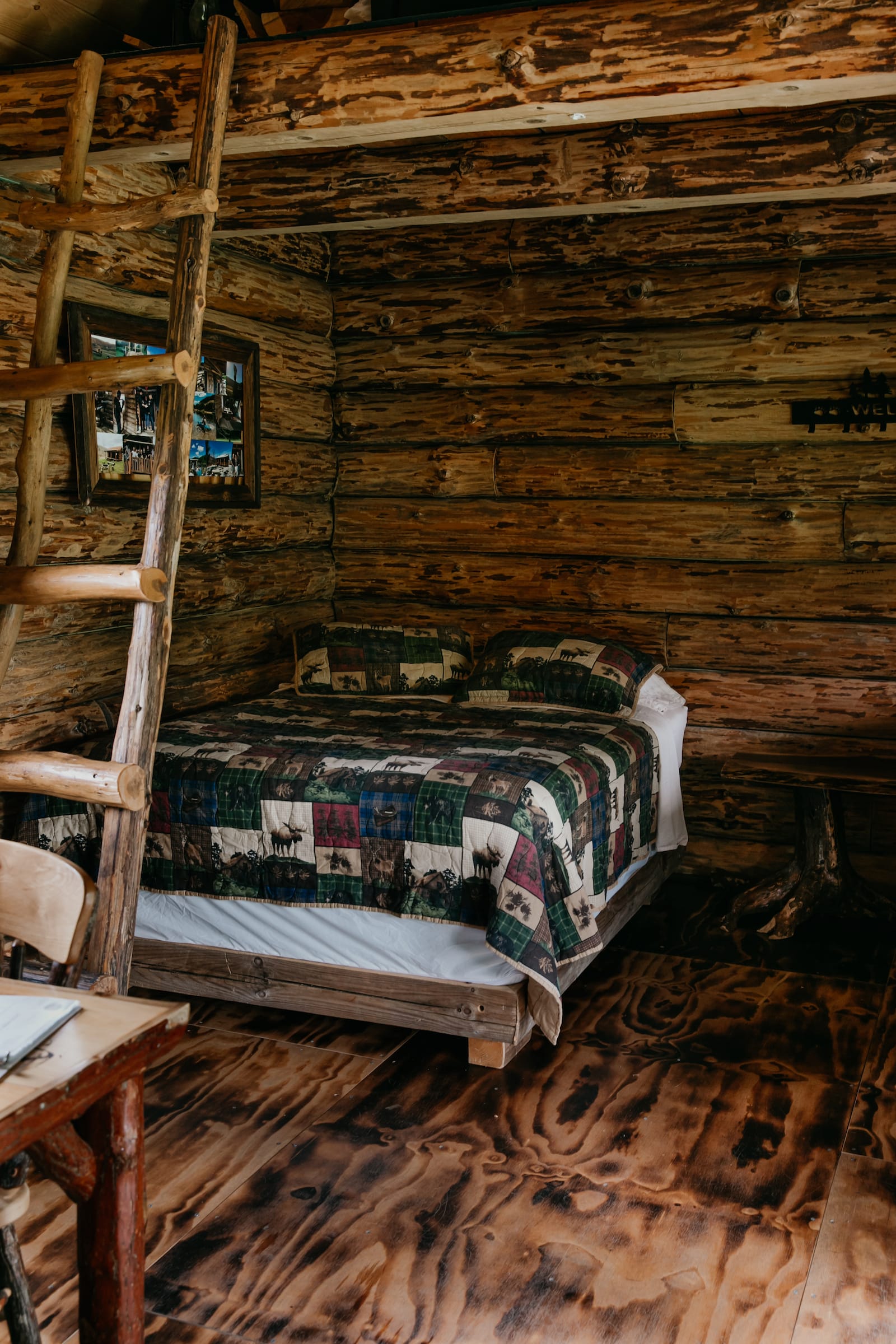Clara Creek Company, Rustic log cabin bedroom with a patchwork quilt on the bed and a wooden ladder. Bed and breakfast home interior.
