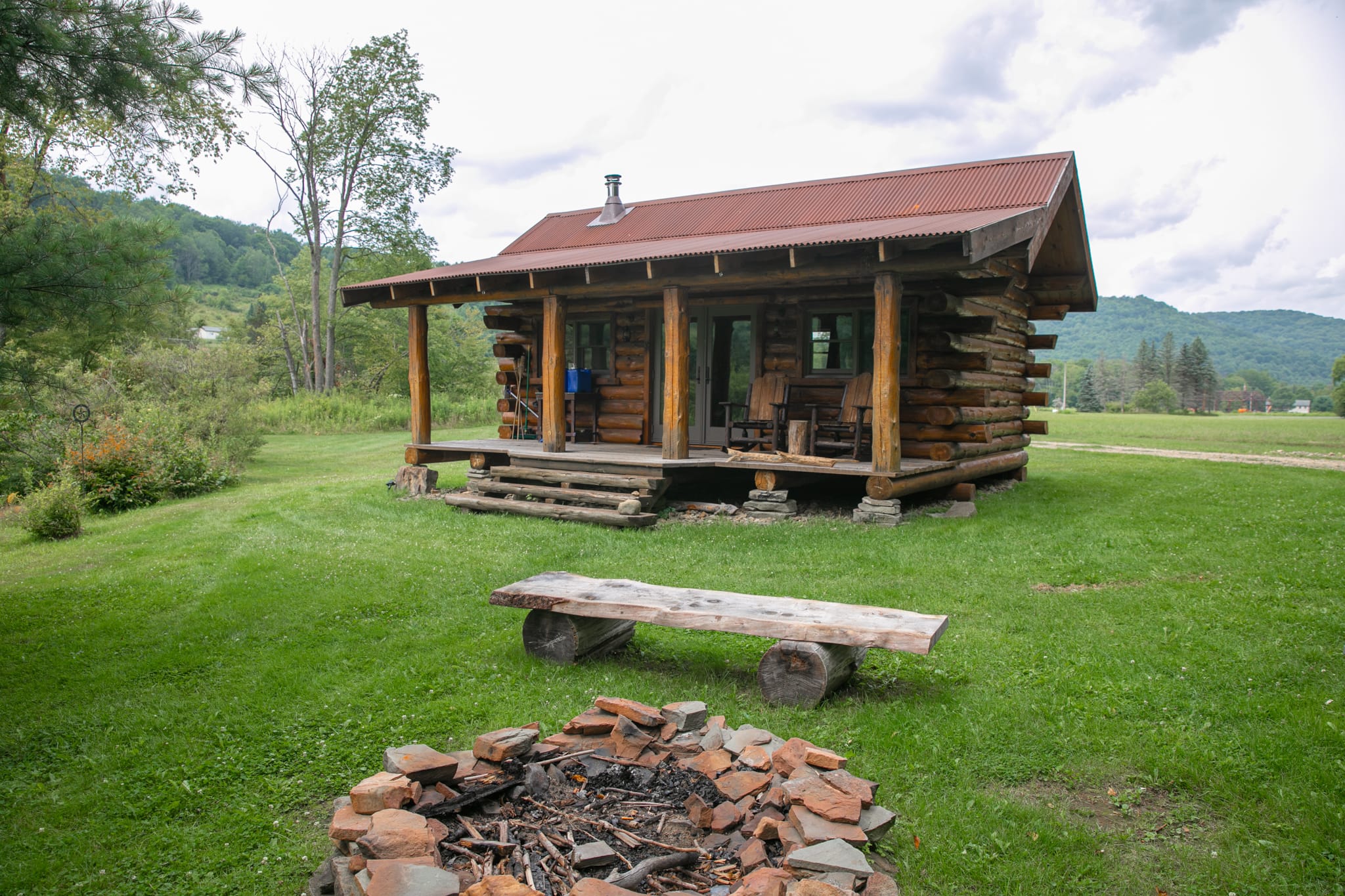 57A4020 - Clara Creek Clara Creek Company, Log cabin home with a stone fire pit and wooden bench.