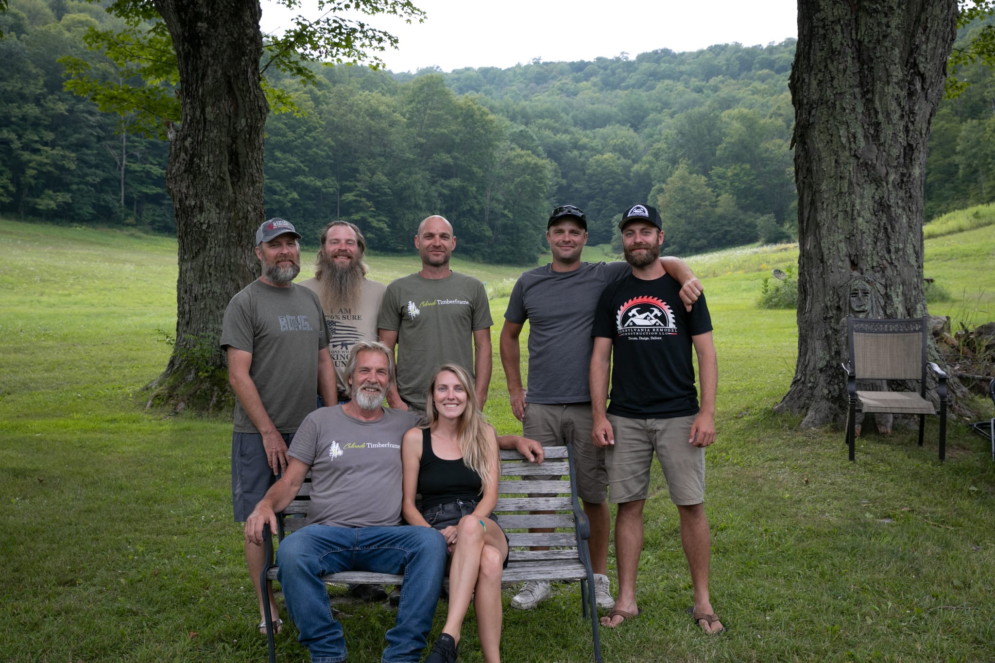 57A4133 Clara Creek Company, Group photo of the team behind Timberframe, standing and sitting in a field with trees.